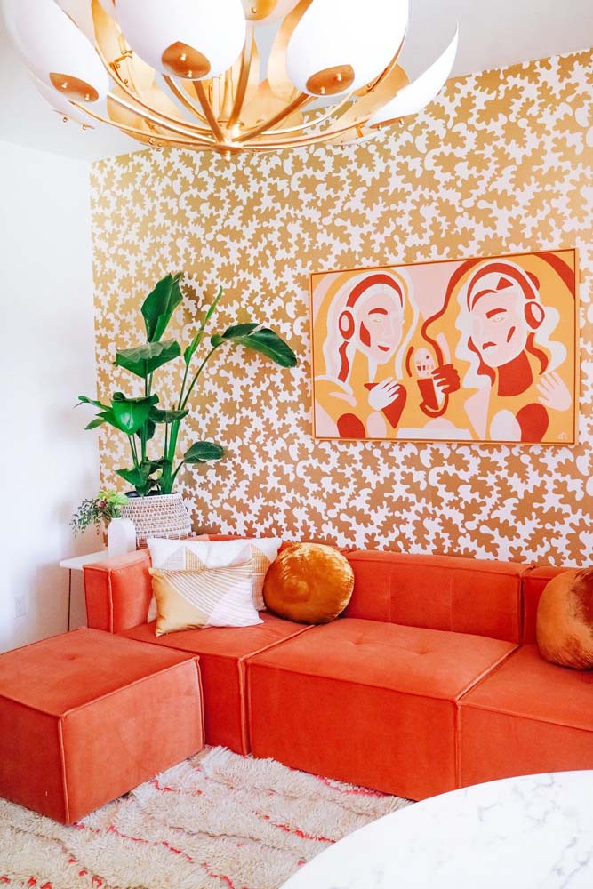 Para combinar com o sofá laranja, um papel de parede para sala de estar com toque de dourado