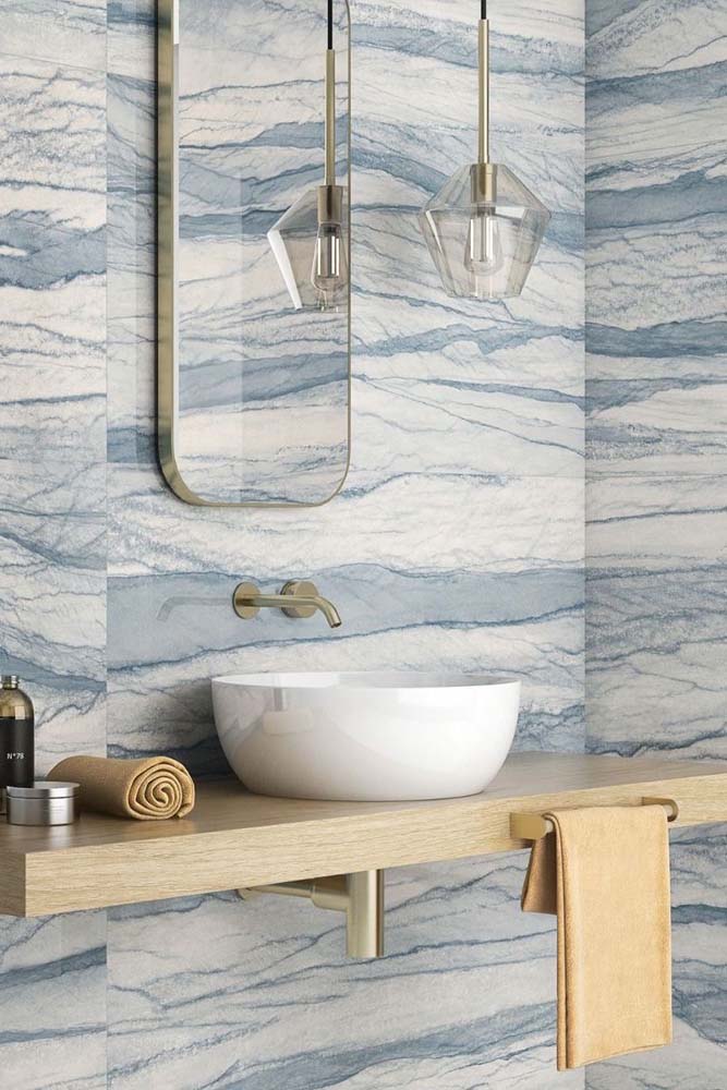 Porcelanato marmorizado branco e azul para o banheiro. Os detalhes em dourado completam o projeto